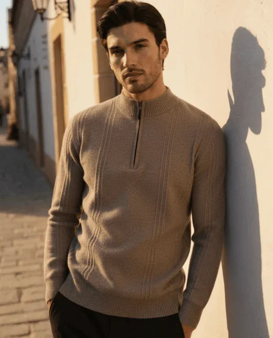 Man wearing beige zip sweater posing outdoors in sunlight against a wall on a street