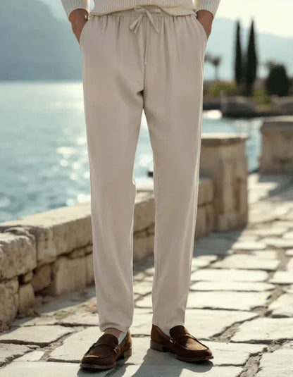 Man wearing beige drawstring pants and loafers by a waterfront stone walkway