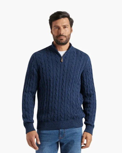 Man wearing a blue cable knit zip sweater and blue jeans on white background