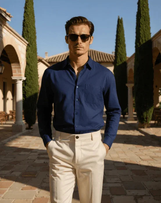 Man in navy dress shirt and cream trousers posing outdoors in Mediterranean courtyard