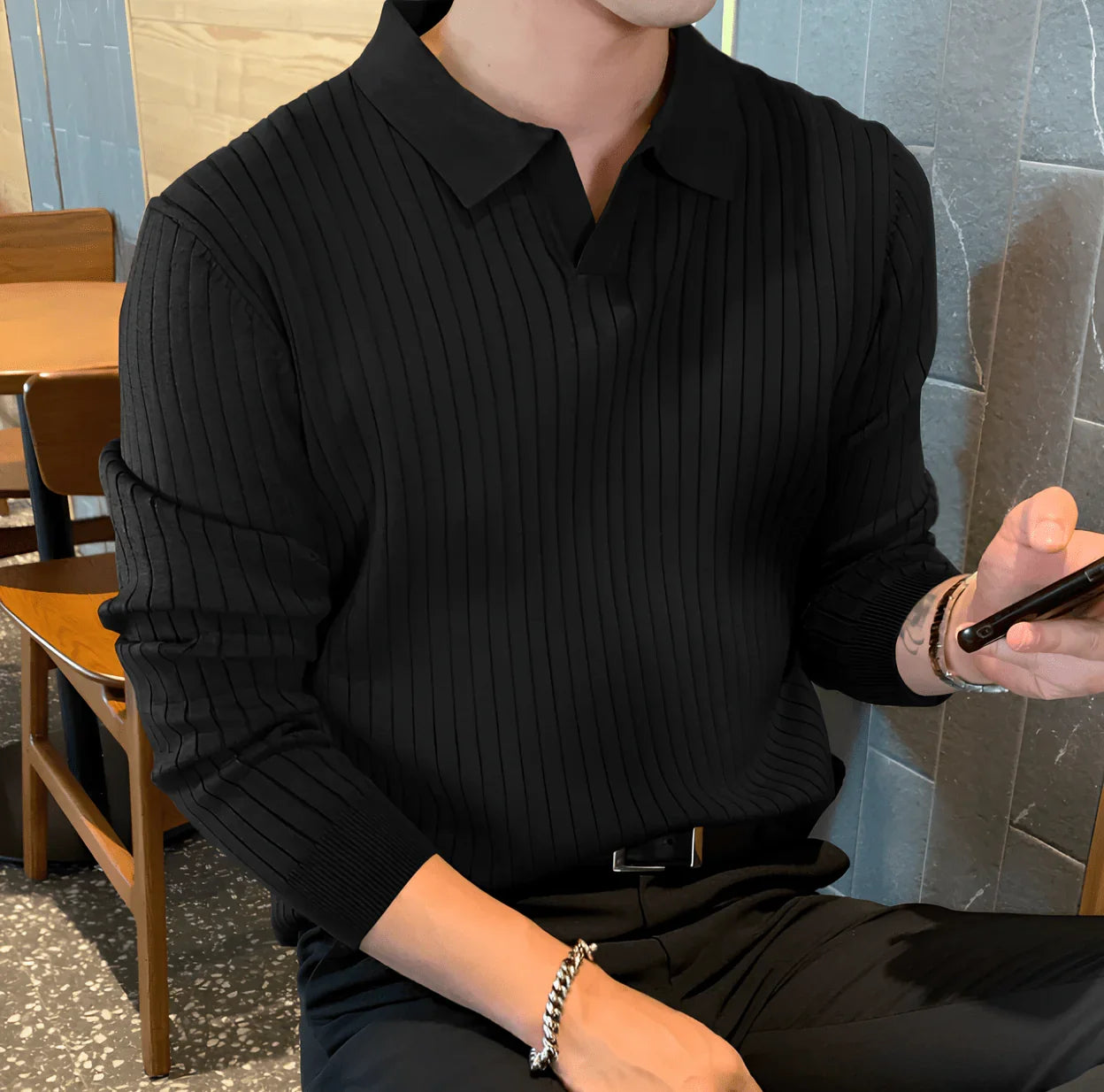 Man in black ribbed knit sweater with collar sitting in modern cafe holding phone